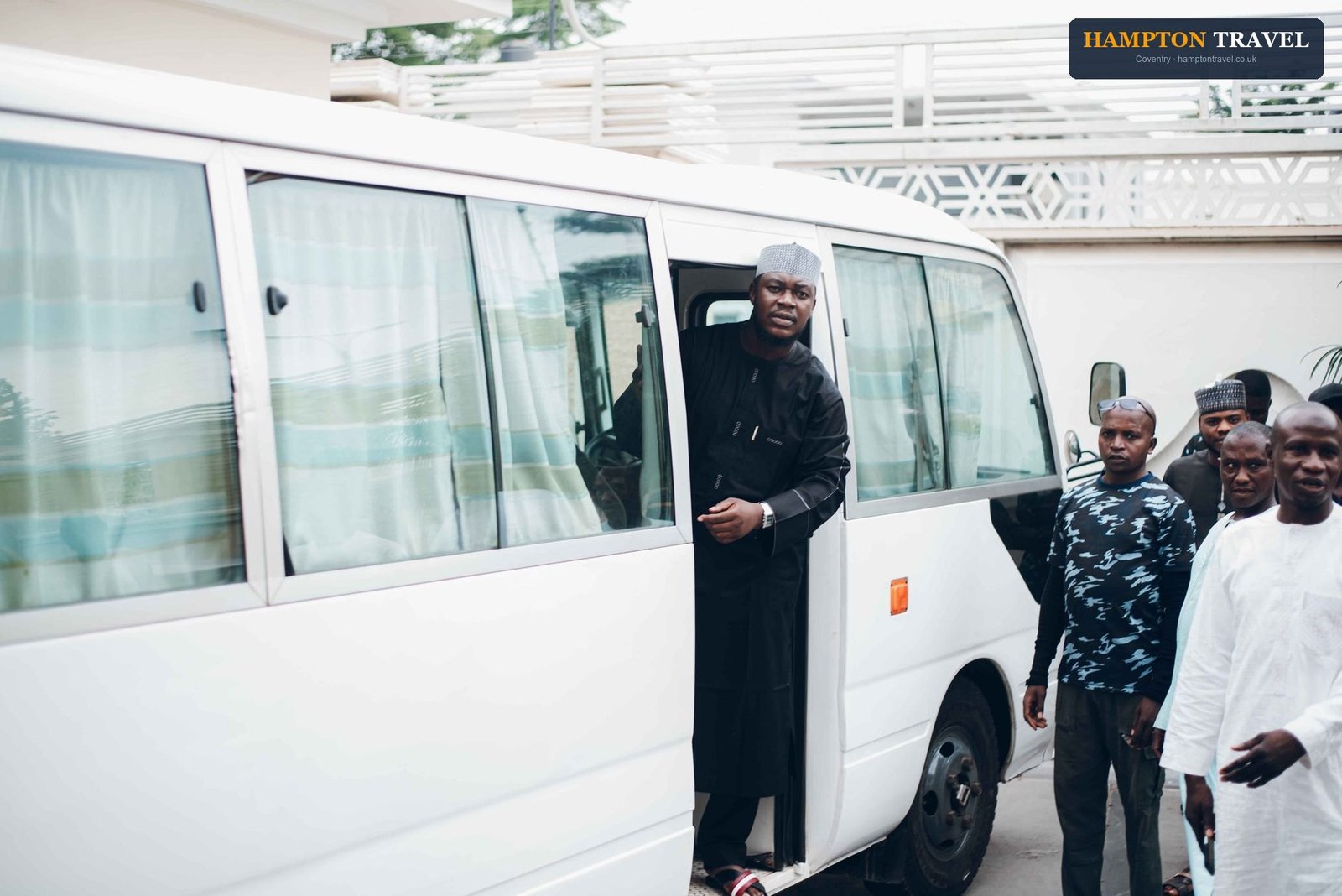 A group of men enter a white minibus parked outdoors, dressed in various attires.